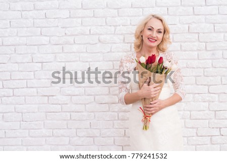 An adult woman posing near a bright wall with flowers. She is a confident woman. She looks very good.