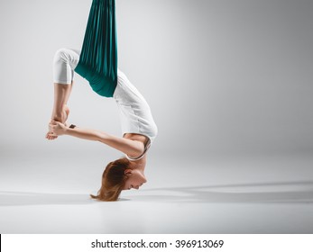An adult woman practices different inversion - anti-gravity yoga positions in a bright well lit studio. 