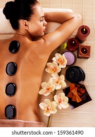 Adult woman relaxing in spa salon with hot stones on body. Beauty treatment therapy