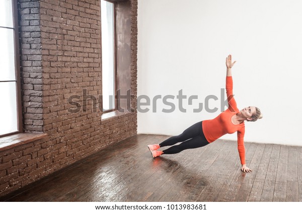 Adult woman in\
side plank pose at yoga class, Vasisthasana exercise. Female\
balancing  indoors at fitness\
gym