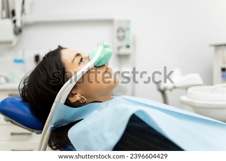 An adult woman sits in a dentist's office wearing a nasal mask to inhale nitrous oxide. Dentist fear concept. Feeling of relaxation with laughing gas. Visit a dentist with relaxation.
