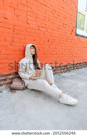 Adult woman sits on the floor with a phone in her hands and a thermo mug with a drink. Wellness concept.