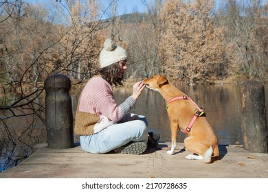 Adult Woman Sitting Next To Pet Dog On Lake Dock In Forest