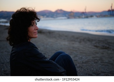 Adult woman sitting on the beach looking at the sea during sunset one winter day