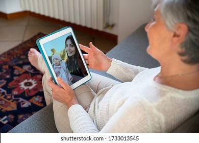 Adult woman sitting on sofa video calling her daughter and her child girl with tablet - In isolation from the virus quarantine, Covid-19 a grandmother talks to her grandson - Concept of Coronavirus - Powered by Shutterstock