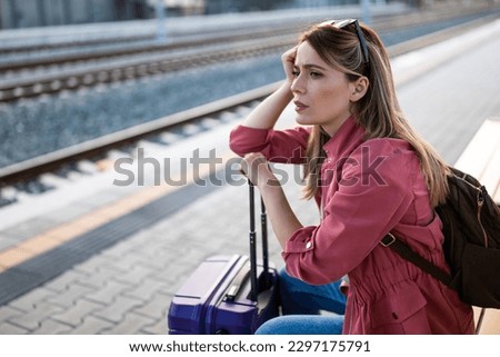 Adult woman is sitting at railway station and waiting for arrival of train.