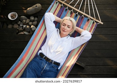 Mujer adulta durmiendo en una hamaca en la terraza de la cubierta durante la soleada tarde de verano. Concepto de hábito saludable de la siesta.