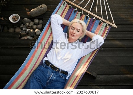 Adult woman sleeping in hammock on deck terrace during sunny summer afternoon. Healthy nap habit concept.