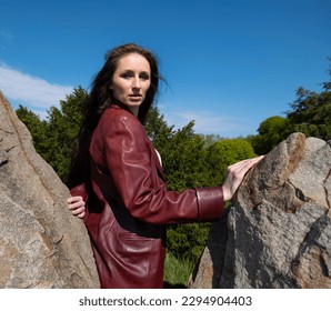 An adult woman stands on a rocky ledge and looks up at the sky. She enjoys a day of leisurely activity alone. American woman in leather jacket between stones - Powered by Shutterstock