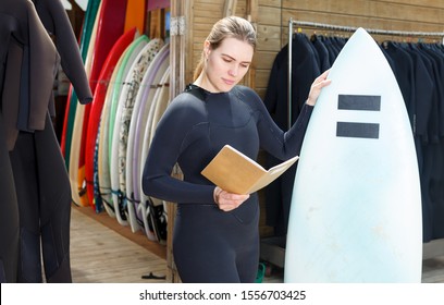 Adult woman surf club instructor in wetsuit, standing outdoor with surfboard - Powered by Shutterstock