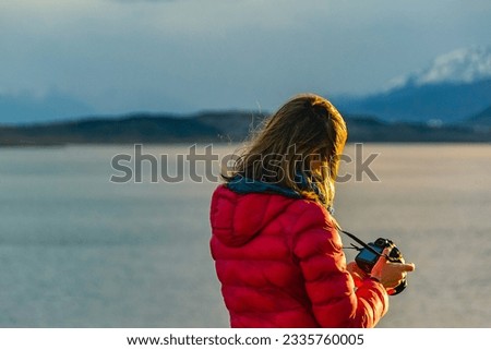 Adult woman taking photos with reflex camera at border of lake, ushuaia, tierra del fuego, argentina