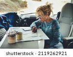 Adult woman travel alone with camper van motorhome and enjoy adventure and freedom vanlife lifestyle. Female people tourist with van transport. Cute lady planning destination on a guide paper map