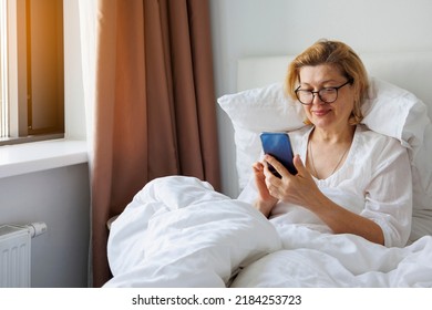 An Adult Woman Uses A Mobile Phone. Lying In The Bedroom Bed.