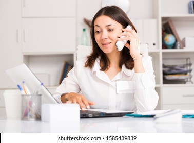 Adult woman working with  laptop and talking by smartphone  in office 