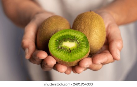 Adult woman's hand holding a ripe green kiwi fruit cut in half ready to eat. Concept of fruit rich in vitamins and healthy eating. - Powered by Shutterstock