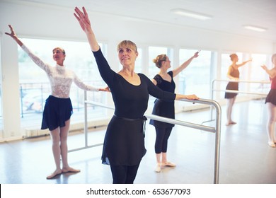 Adult women smiling and standing with hands up performing a gymnastics in ballet class.