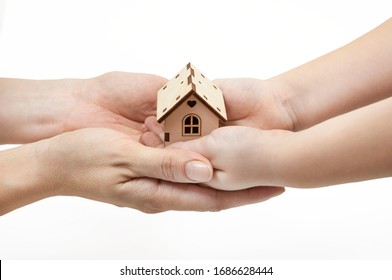 Adults And Children's Hands Holding A Wooden House, Family Home, Homeless Housing And Home Insurance Concept, International Family Day, Foster Care, On A White Background.