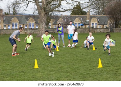 Adults on grassed area with school children supervising a football training session, Everyone can be seen running around cones. School building can be seen in the background. - Powered by Shutterstock