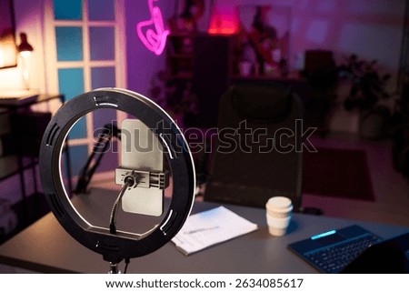Advanced studio setup with recording equipment, smartphone on stand, ring light. Features ergonomic furniture and electronic devices, with purple neon light