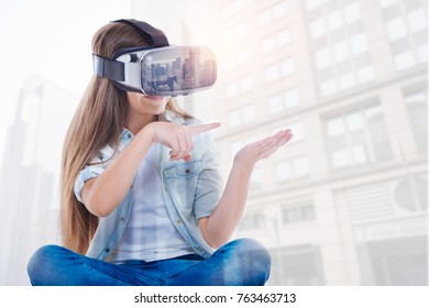 Advanced Technology. Funny Kind Interested Girl Pointing With Her Finger While Sitting And Wearing VR Glasses