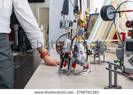 Advanced white and gray walking educational robot displayed on a table at an educational exhibition or makerspace. Complex robotics project with multiple joints and mechanisms.