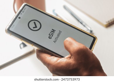 Advantage of embedded SIM connection for network services concept. A person's mobile phone displaying eSIM activated successfully.