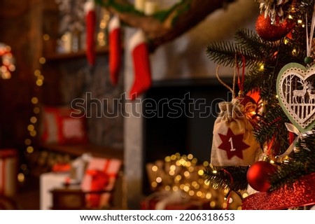 Advent calendar in the form of an eco bag hangs on the Christmas tree against the background of the Christmas room with a fireplace and Santa's boots.Christmas background. Advent calendar.