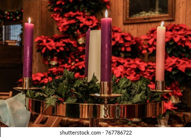 Advent Candles In A Church With Poinsettia Plants In The Background.