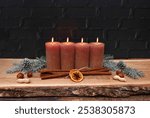 Advent decoration: Arrangement for the fourth Advent: Decoration with four brown Advent candles and Christmas decorations in front of a black wall with space for text.