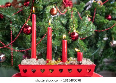 Advent greeting card. Four red burning candles in a beautiful candlestick. Decorated Christmas tree background. Christmas Holiday in Christian countries. Swedish traditions.