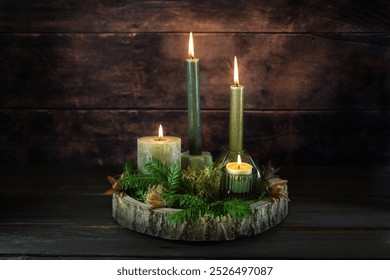 Advent wreath alternative made from a slice of tree, four variations of green candles, moss and twigs against a dark rustic wooden background with copy space, selected focus - Powered by Shutterstock