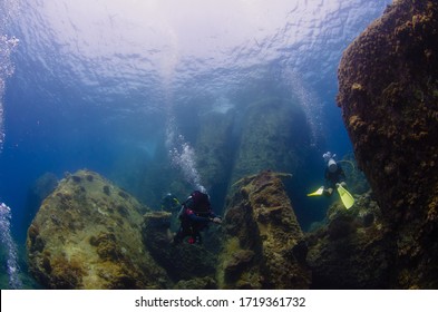 Adventure deep dive at Perhentian Island. Excellent underwater visibility showing divers ascending from the larger boulder formation towards the pinnacle.