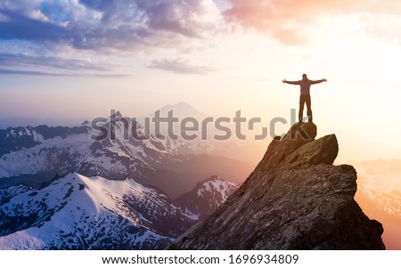 Adventure, Explore and Lifestyle Concept Composite. Adventurous Man Hiker With Hands Up on top of a Steep Rocky Cliff. Sunset or Sunrise. Landscape Taken from Washington, USA.