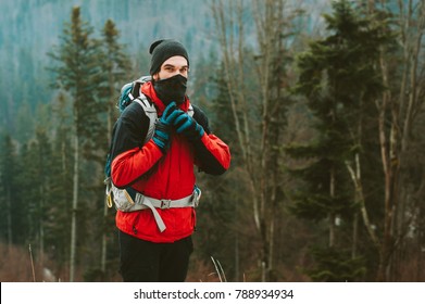 Adventure Man Hiking Wilderness Mountain With Backpack, Outdoor Lifestyle Survival Vacation. Portrait Of Mountaineer In Snow Mask. A Man In Bright Sportswear Trekking In A Winter Forest. 