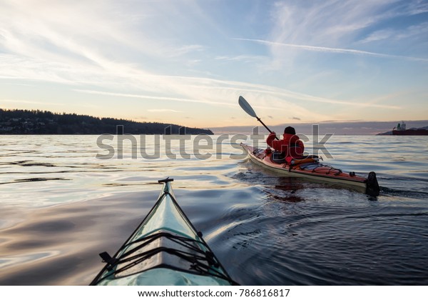 Adventure Man on a Sea Kayak is kayaking\
during a vibrant and colorful winter sunset. Taken in Vancouver,\
British Columbia, Canada. Adventure, Vacation\
Concept