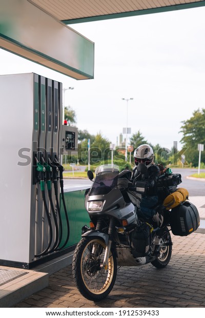 The adventure motorcycle with bags is at a\
gas station. Fuel quality, price and distance concept. Payment\
systems in different countries. Vertical\
photo