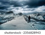 Adventure of mountaineer standing on top of snowy mountain with dark stormy sky in winter on Segla mount at Senja Island, Norway