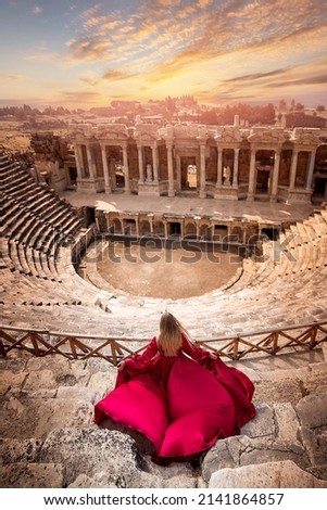 Adventure photo tourist woman in red dress on background Amphitheater in Hierapolis ancient city Pamukkale Turkey.