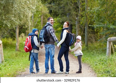 adventure, travel, tourism, hike and people concept - happy family walking with backpacks in woods and looking back
