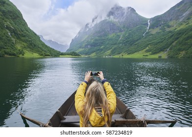 Adventure Woman In Row Boat Taking Photo On Smart Phone Of Beautiful Fjord Lake For Social Media