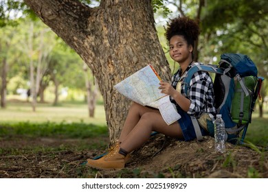 Adventure, Young women teenager ethnic African American black skin wearing plaid shirt and her backpack sitting at tree base looking down on the map travel in her hand in natural light of the forest, - Powered by Shutterstock