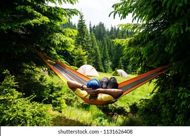 Adventurer relaxes in hammock on the green mountain meadow among fir trees and admires view. Epic travel in the mountains. Back view. - Powered by Shutterstock