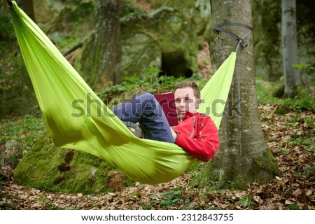 An adventurer rests in a hammock. After the expedition, the tourist rests in a hammock, reads a book in the forest, basking in the warmth of a sunny day.