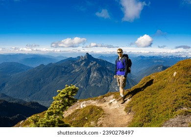 Adventurous athletic male hiker standing on a hiking trail on top of a rugged mountain at at the camera smiling, in the Pacific Northwest with jagged mountains in the background.
 - Powered by Shutterstock