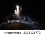 Adventurous athletic male standing in a lava tube looking at the sunlight shinning down into the cave through holes in the ceiling.