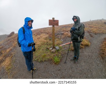 Adventurous Athletic Rain Soaked Male Hikers Standing On A Trail Facing The Camera Smiling In Early Spring On A Cloudy Day In The Pacific Northwest.
