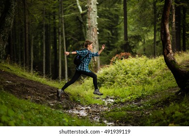 Adventurous And Athletic Woman Runs And Jumps Over A Creek In A Forest