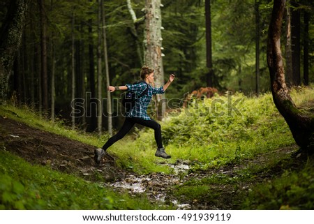adventurous and athletic woman runs and jumps over a creek in a forest