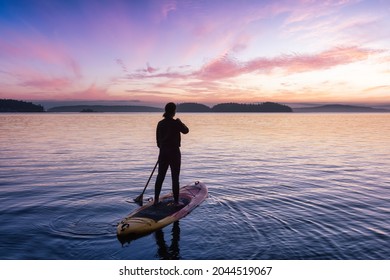 Adventurous Caucasian Adult Woman On A Stand Up Paddle Board Is Paddling On The West Coast Of Pacific Ocean. Sunny Sunrise Sky Art Render. Victoria, Vancouver Island, BC, Canada.