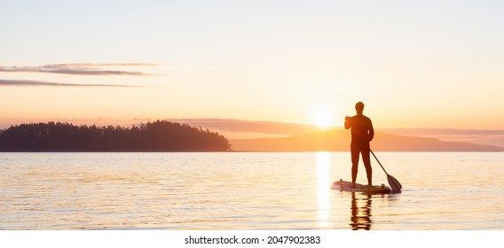 Adventurous Caucasian Adult Woman On A Stand Up Paddle Board Is Paddling On The West Coast Of Pacific Ocean. Sunny Sunrise. Victoria, Vancouver Island, BC, Canada.